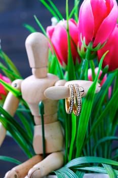 Wooden figure holding two golden wedding ring resting with fake pink tulip flower