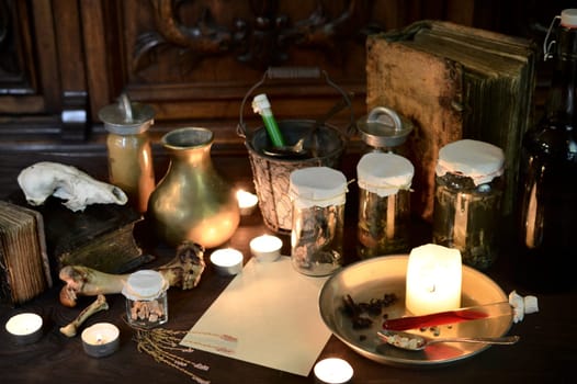 eerie witches' kitchen with lot of ingredients for a potion, a blank sheet of paper for the recipe or greetings and ancient gruesome jars dark with only candlelight for Halloween