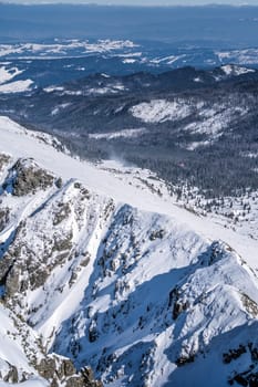 Rescue helicopter flying over pine forest in the valley. Snow capped mountain peaks of Tatra Mountains in winter, Bukowina Tatrzanska, Poland