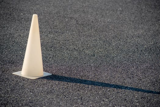 Full frame image with copy space shot in natural light. White plastic cone glows in golden hour sun and casts a long shadow on the black asphalt.