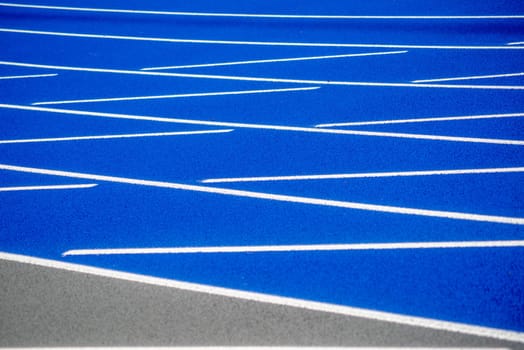 Full frame image in natural light of textured surface of a clean, new outdoor blue running track with white lines and copy space.