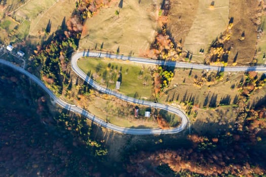 Aerial view of road in beautiful autumn forest at sunset.