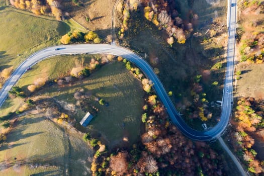 Aerial view of road in beautiful autumn forest at sunset.