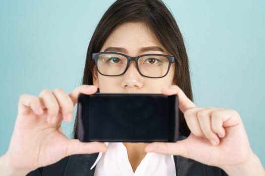 Young women in suit holding her smartphone standing against blue background