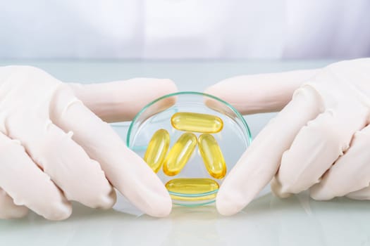 Close up Scientist hands putting in nitrile latex gloves holding Omega 3 capsule in labcoat wearing nitrile gloves, doing experiments in lab