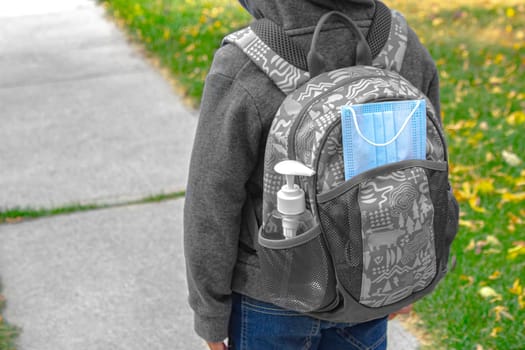 A Kid with a school bag with a face mask and hand sanitizer on a pocket