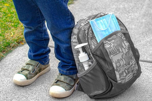Kids shoes next to a school bag with a face mask and hand sanitizer