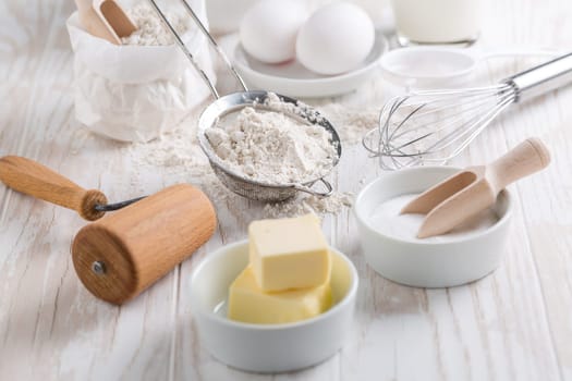 Spelt flour, sugar with baking ingredients and kitchen utensils on white wooden table.