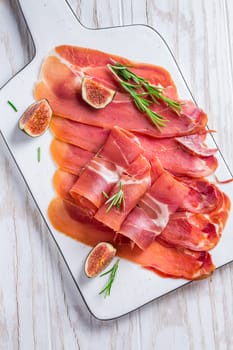 Delicious Serrano ham with fresh figs and rosemary on white cutting board