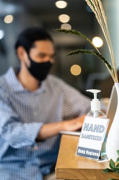 Signage of Hand Sanitizer around office for hygiene practice after reopen with blurred background of business people working and wear face mask in new normal office to prevent covid-19 virus spreading
