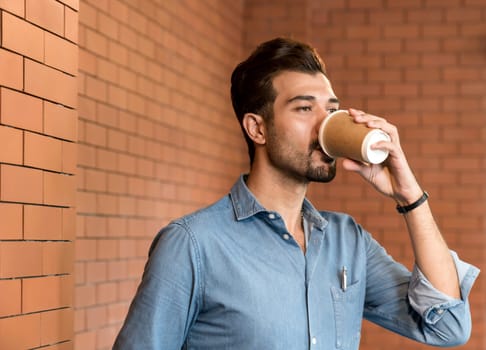 Portrait of middle east caucasian businessman drinking coffee from takeout disposable coffee cup and clipboard in meeting room after lunch break.