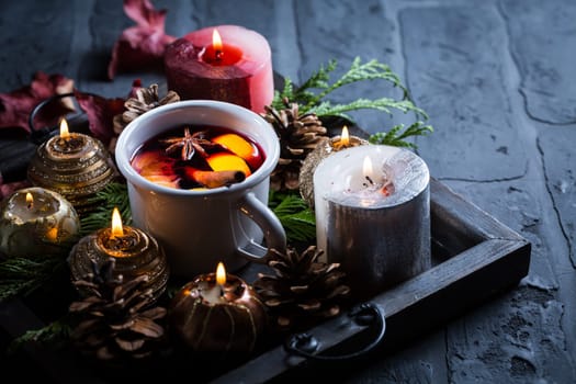 Spicy mulled wine with orange, cinnamon and anise in mug with Christmas candles