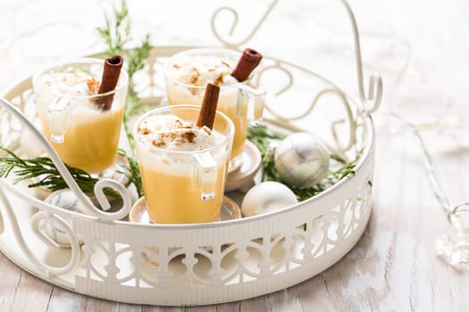 Eggnog with cinnamon and nutmeg for Christmas and winter holidays. With Xmas decorations on wooden background.