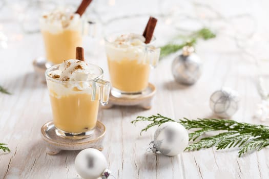 Eggnog with cinnamon and nutmeg for Christmas and winter holidays. With Xmas decorations on wooden background.