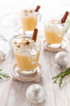 Eggnog with cinnamon and nutmeg for Christmas and winter holidays. With Xmas decorations on wooden background.