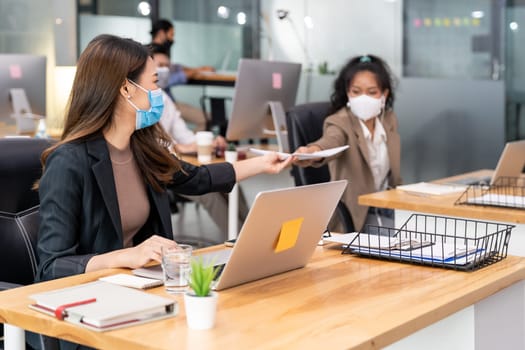 Group of interracial business worker team wear protective face mask in new normal office with social distance practice with hand sanitiser alcohol gel on table prevent coronavirus COVID-19 spreading