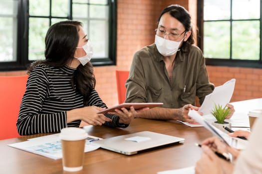 Group of asian business person team meeting and brainstorm in meeting room after office reopen, they wear protective face mask as new normal practice to prevent coronavirus infection.