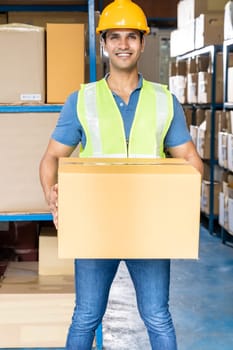 Portrait of Indian warehouse worker hold cardboard box packaging in warehouse distribution center environment. Using in business warehouse and logistic concept.