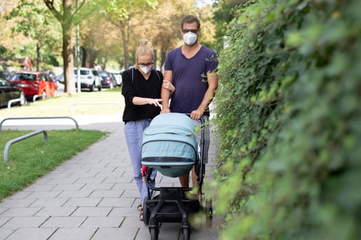 Worried young parent walking on empty street with stroller wearing medical masks to protect them from corona virus. Social distancing life during corona virus pandemic.