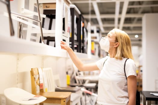 New normal during covid epidemic. Caucasian woman shopping at retail furniture and home accessories store wearing protective medical face mask to prevent spreading of corona virus.