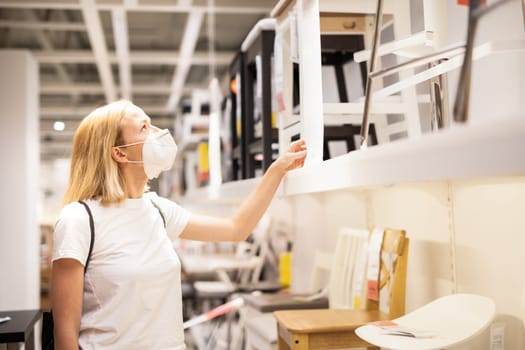 New normal during covid epidemic. Caucasian woman shopping at retail furniture and home accessories store wearing protective medical face mask to prevent spreading of corona virus.