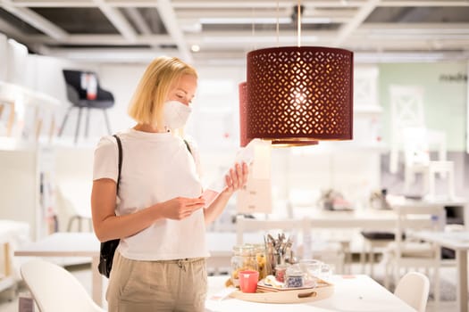 New normal during covid epidemic. Caucasian woman shopping at retail furniture and home accessories store wearing protective medical face mask to prevent spreading of corona virus.