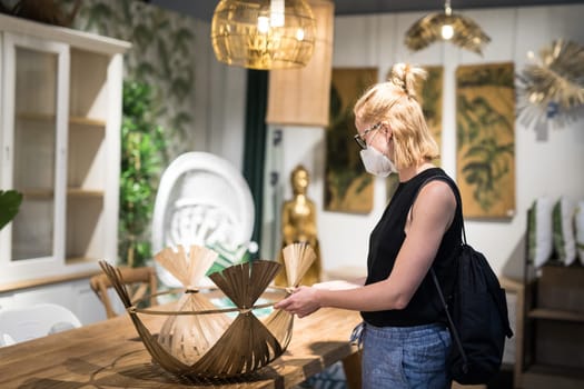 New normal during covid epidemic. Caucasian woman shopping at retail furniture and home accessories store wearing protective medical face mask to prevent spreading of corona virus.