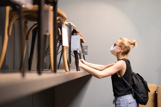 New normal during covid epidemic. Caucasian woman shopping at retail furniture and home accessories store wearing protective medical face mask to prevent spreading of corona virus.