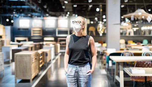 New normal during covid epidemic. Caucasian woman shopping at retail furniture and home accessories store wearing protective medical face mask to prevent spreading of corona virus.