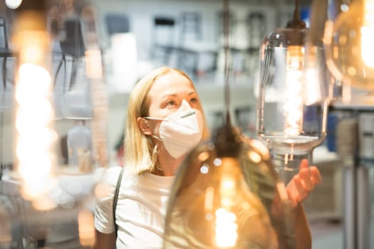 New normal during covid epidemic. Caucasian woman shopping at retail furniture and home accessories store wearing protective medical face mask to prevent spreading of corona virus.