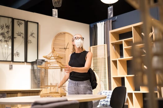 New normal during covid epidemic. Caucasian woman shopping at retail furniture and home accessories store wearing protective medical face mask to prevent spreading of corona virus.
