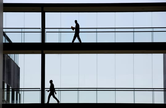 Silhouette view of two businessmen in a modern office building interior with panoramic windows.