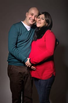 happy pregnant couple posing on dark background
