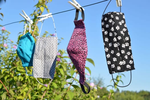 a lot of different colorful self made corona face masks out of fabric hanging on a clothesline for drying