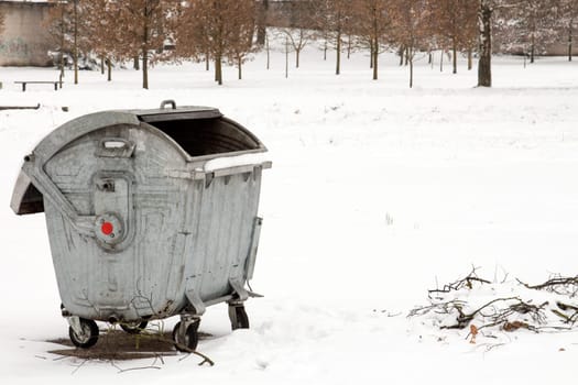 Opened metal garbage container in a winter park