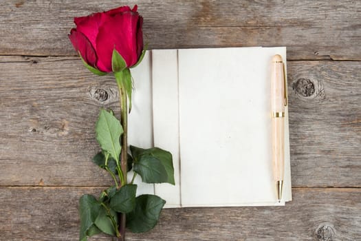 Old rose and blank paper sheets with pen on wooden background