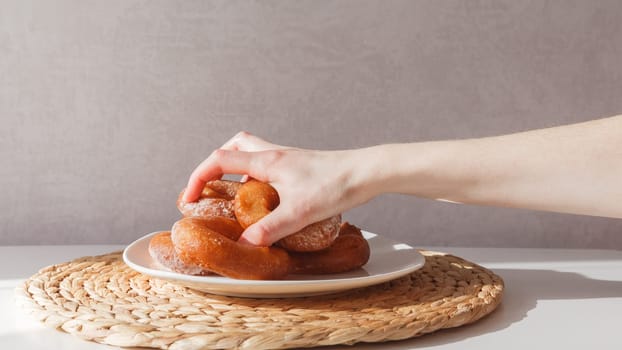 Glutton girl grabs donuts from a plate. Girls hand and plate with donuts.