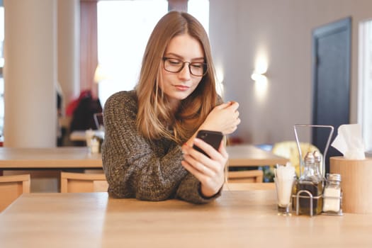 Charming woman with beautiful smile reading good news on mobile phone during rest in coffee shop