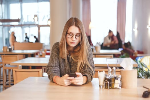 Charming woman with beautiful smile reading good news on mobile phone during rest in coffee shop