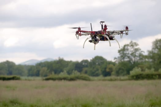 Large hex copter camera drone hovers in front of a rural back ground of the malvern hills. Autonomous FPV modern flight, gimbal stabilized camera
