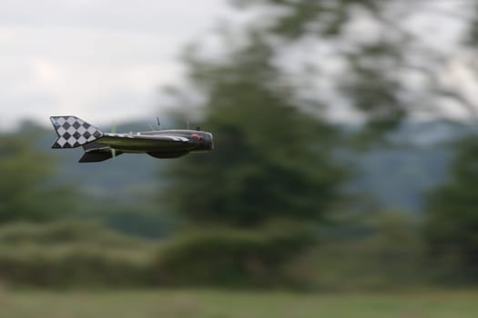 Pan shot technique creates a blurred background as this remote control delta FPV drone flies pas at high speed. Rural background and racing pattern.