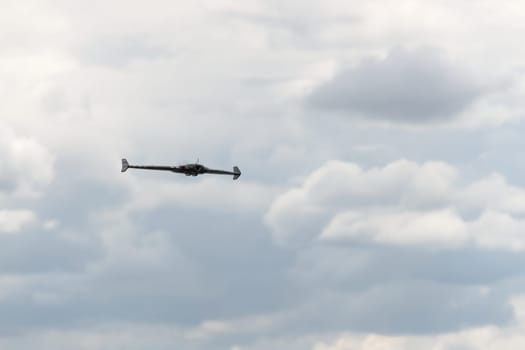 Gentle fluffy clouds in a grey sky form the background behind this FPV first person view flying wing drone. Selective focus and head on view.
