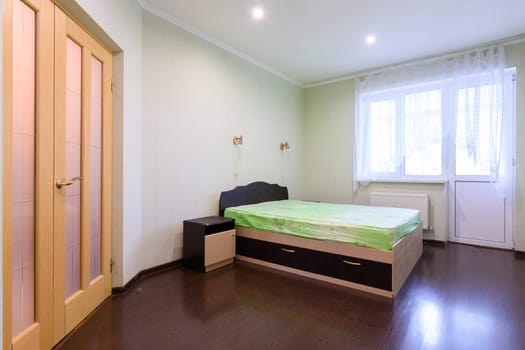 Bedroom interior with a bed in the middle and a large window opening onto a balcony
