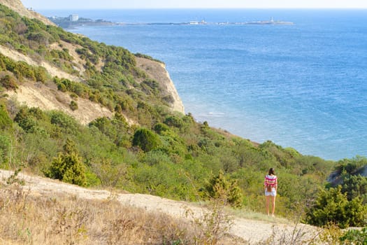 A girl stands on a hill and looks into the distance at the sea