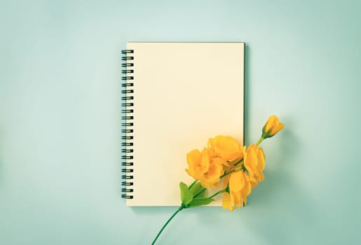 Spiral Notebook or Spring Notebook in Unlined Type and Orange Flowers at Bottom Right on Blue Pastel Minimalist Background. Spiral Notebook Mockup on Center Frame in Vintage Tone