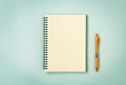 Spiral Notebook or Spring Notebook in Unlined Type and Orange Pen on Blue Pastel Minimalist Background. Spiral Notebook Mockup on Center Frame in Vintage Tone