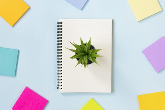Spiral Notebook or Spring Notebook in Unlined Type and Multi Color Sticky Note and Office Plant on Blue Pastel Minimalist Background. Spiral Notebook Mockup on Center Frame