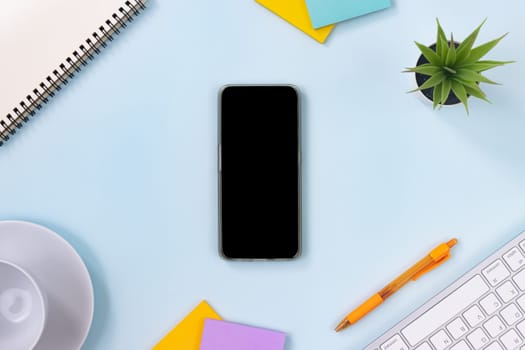 Vertical Mobile Phone or Smartphone and Office Supplies as Keyboard,Pen,Sticky Note,Office Plants,Spiral Notebook,Coffee Cup on Modern Clean Creative Office Desk or Table on Top View or Flat Lay