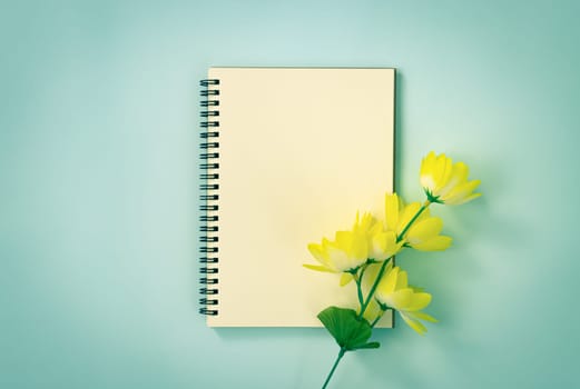 Spiral Notebook or Spring Notebook in Unlined Type and Yellow Flowers at Bottom Right on Blue Pastel Minimalist Background in Vintage Tone