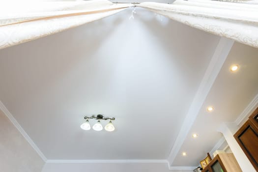 Two-level ceiling with a small chandelier in the interior of the room